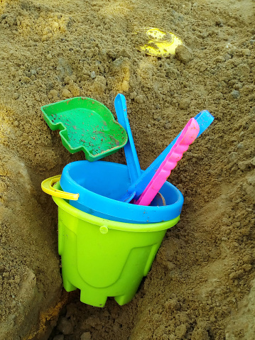 Colorful toys are forgotten in the sandbox. Plastic tools: shovel and pail. Close-up.