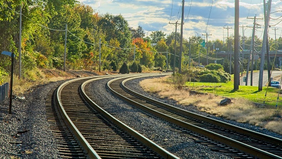 Railroad track through curve alignment under bright afternoon sunlight early autumn tree color