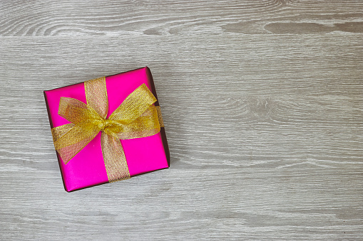 pink gift box with golden ribbon on gray wood background