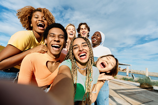 Frontal close-up view of a group of happy and excited multicultural friends taking a selfie outdoors
