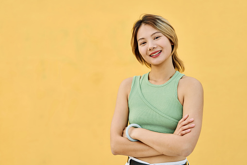 Proud chinese young woman smiling at camera standing with arms crossed