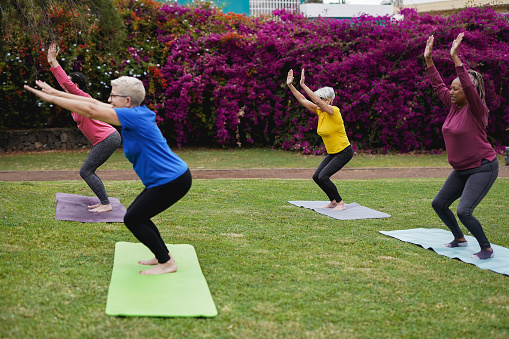 Multiracial women with different ages doing yoga sport exercise at city park - Healthy lifestyle - Focus on the senior woman with yellow shirt