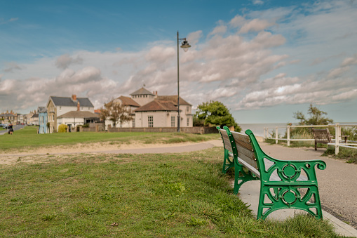 Isolated painted wrought iron public bench seen near the cliff top of a famous, Suffolk seaside town. The town can be seen on the left.