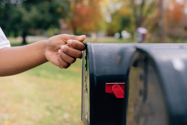 Close-up shot of a Black woman's hand opening a mailbox in the suburbs Part of a Series: African American / Black Woman Receiving a Mail-In Ballot to Vote from Home in the USA Presidential or Senatorial Election. Photo taken in Tennessee, USA. us mailbox stock pictures, royalty-free photos & images