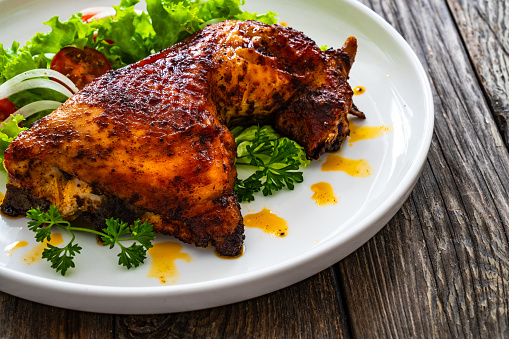 Roasted chicken thigh with fresh vegetables on wooden table