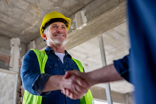 Happy architect handshaking a construction worker at a building site - construction industry concepts