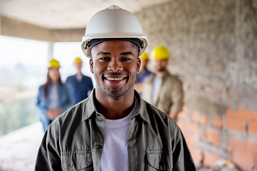 Happy African American man working at a construction site with a group of workers and looking at the camera smiling