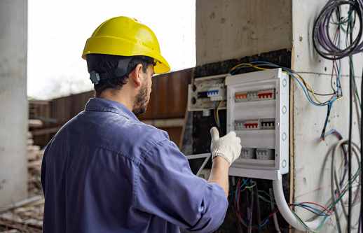 Electrician working at a construction site checking the wiring of a building and using a digital tablet