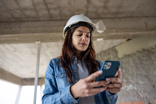 Portrait of an architect working at a construction site and texting on her cell phone - housing development concepts