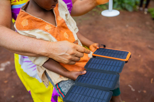 nahaufnahme eines solarpanels, das von einem afrikanischen kind gehalten wird, während seine mutter erklärt, wie es funktioniert - energy fuel and power generation futuristic solar energy stock-fotos und bilder
