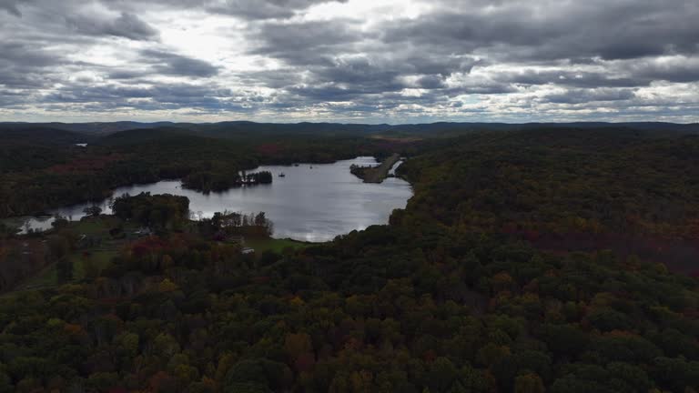 Aerial view of the countryside in Stormville, New York on a cloudy day in autumn with Black Pond in view. The camera dolly in and truck right towards the pond with an abandoned aircraft runway.