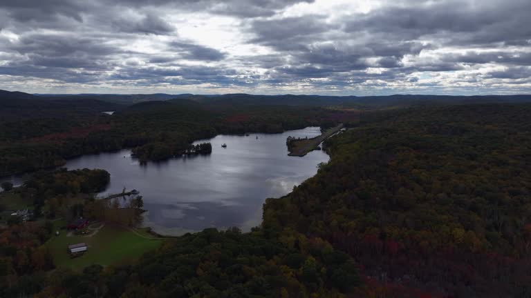 Aerial view of the countryside in Stormville, New York on a cloudy day in the fall with Black Pond in the shot. The camera dolly in and truck right by the pond with an abandoned aircraft runway.