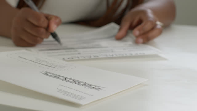 Static lock-down shot of a Black woman filling out a mail-in ballot to vote at home for Presidential, Senatorial, Congressional, or local election