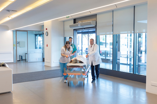 The paramedics take the patient from the ambulance to the hospital on a stretcher. Two paramedics and a patient. Modern ambulance. Emergency room entrance of a large hospital.