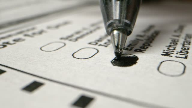 Extreme close-up macro video of a ballpoint pen filling in a mail-in voting ballot at home for Presidential, Senatorial, Congressional, or local election