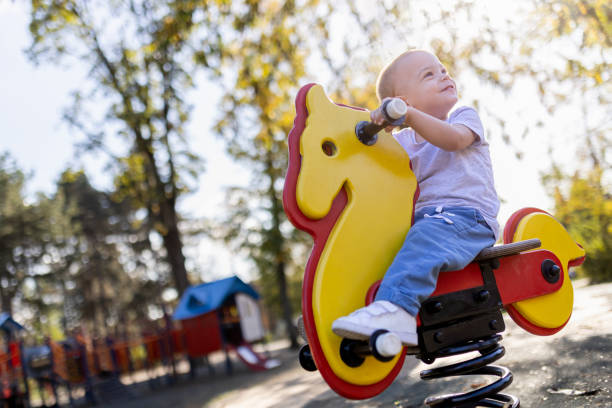 Young happy boy riding rocking horse at the park. Portrait of cute boy playing on bouncy horse at the playground. playground spring horse stock pictures, royalty-free photos & images