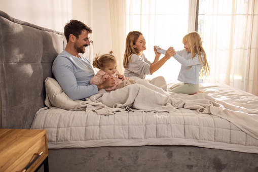 Happy family with two kids playing in bed in the morning