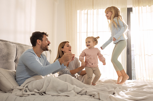 Happy family with two kids playing in bed in the morning