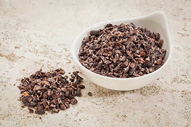 raw cacao nibs small ceramic bowl of  raw cacao nibs  against a ceramic tile background with a copy space cacao nib stock pictures, royalty-free photos & images