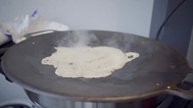 A thin pancake is baking on the big steelpan in the grill. Making food outside at the terrace in scandinavia.