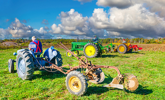 Sandwich, Massachusetts, USA- October 28, 2023-   Three men line up their colorful antique tractors at the edge of a agricultural field on Cape Cod in preparation of plowing another furrow.