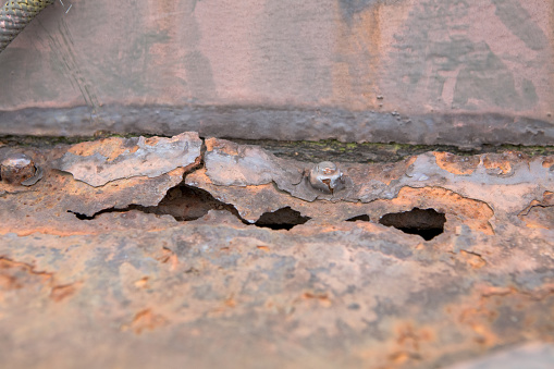 This is a detail image of rust and holes in metal. This could be used for a background or gunge image. Metal that is degraded from age with rust, bolts, and a weld seam.