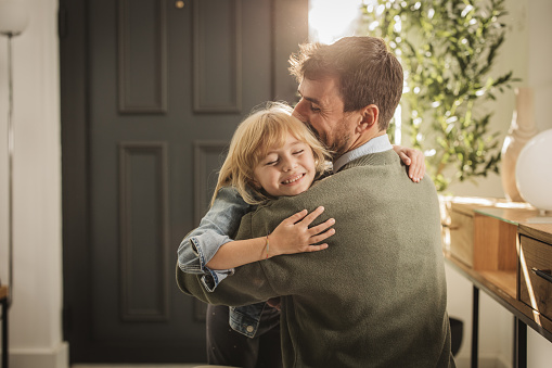 Father embracing his little girl as he enters the house after work.