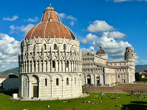 The photo was taken in Pisa, Campo dei Miracoli (UNESCO Heritage Site), on a beautiful autumn day. It shows the Baptistery, Duomo and leaning Tower as seen from the walls, and the surrounding meadows where people are relaxing.