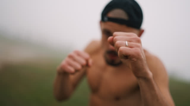 SLO MO Blurred Shirtless Muscular Man Punching on Camera During Boxing Training on Grassy Field in Foggy Weather