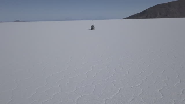 Aerial drone shot of a 4x4 offroad vehicle driving on the Salar de Uyuni salt lake around the isla pescado, fish island, on the biggest salt flat in the world in high altitude of the Andes in the Bolivia.