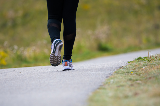 Person running in the park. Woman jogger with running shoes on a park path outdoor healthy lifestyle concept. Running shoes close up of girl jogging on road.