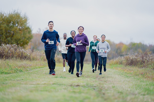A small group of adolescents are seen running in a cross country race.  They are each wearing warm athletic wear as they run on a cool fall day.