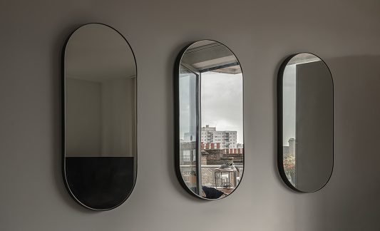 London, UK - Oct 21, 2023 - View of Three Capsula pill shaped mirror on white wall with reflecting of Running shoes hung to dry on the balcony. Space for text, Selective focus.