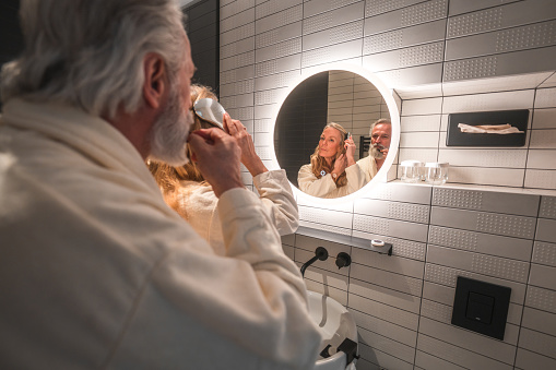 Mature Caucasian couple getting ready in a domestic bathroom. They are wearing bathrobes.