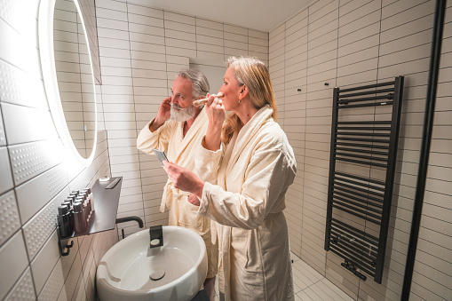 Mature couple performing their morning routine in a domestic bathroom. Combing hair and beard in front of a bathroom mirror.