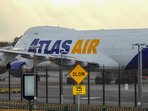 An Atlas Air Boeing B747-47UF plane, registration N409MC, has just arrived from Honolulu as flight QF7558 and parked for unloading at Sydney Kingsford-Smith Airport.  The road speed limit refers to a construction site next to the airport.  This image faces east and was taken from Nigel Love Bridge, Mascot on a cloudy morning at sunrise on 28 October 2023.