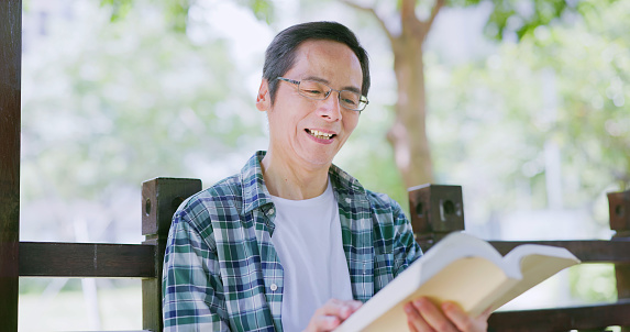 Closeup view of asian elderly male reading a book leisurely and happily in the park