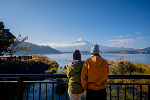 Asian love couple travel together in Japan at Lake Kawaguchiko in autumn with Mount Fuji view.