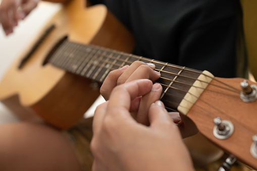 Asian boy playing guitar with mom in the living room for teaching him son play guitar, feel appreciated and encouraged. Concept of a happy family, learning and fun lifestyle, love family ties