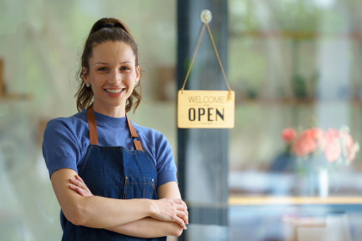A woman who runs a restaurant and coffee shop business stands to welcome confidently with her arms crossed. Hang a sign to open the restaurant. Small business concept.