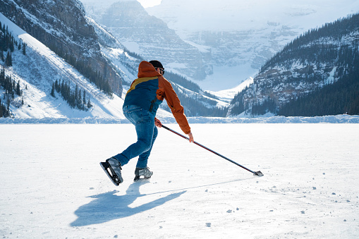 A male skater plays hockey on frozen Lake Louise in winter, Banff National Park, Alberta, Canada