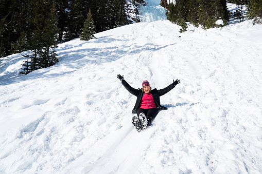 A female slides down a snowy hill at Lake Louise in winter, Banff National Park, Alberta, Canada