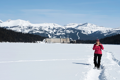 Female hiking across frozen Lake Louise with Fairmont Chateau Inn in the distance on a winter day, Banff National Park, Alberta, Canada