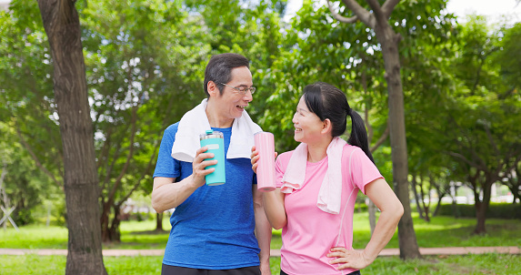 Closeup asian elderly couple happily drinking water after exercising in the park - they feel comfortable physically and mentally