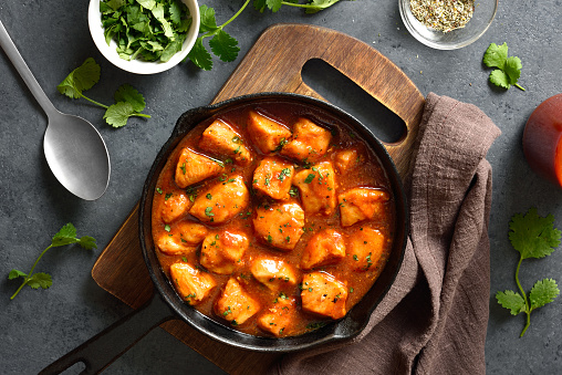 Sweet and spicy chicken bites with sauce in cast iron pan over dark stone background. Top view, flat lay