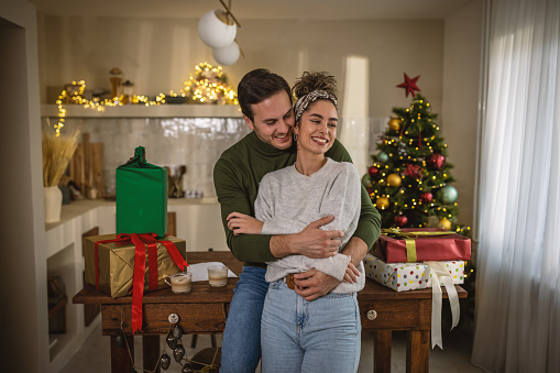 Young couple for Christmas at home. They are standing in front of kitchen island and hugging.