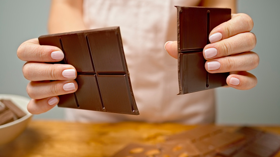 Close-up of woman's hands breaking piece of dark chocolate.