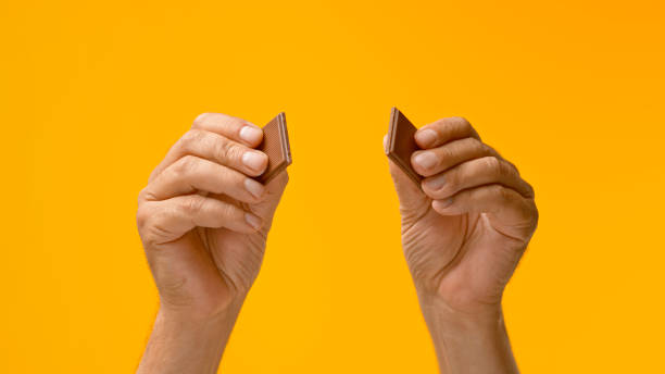 Human hands breaking chocolate Close-up of man's hands breaking chocolate against yellow background. man hand holding candy bar stock pictures, royalty-free photos & images