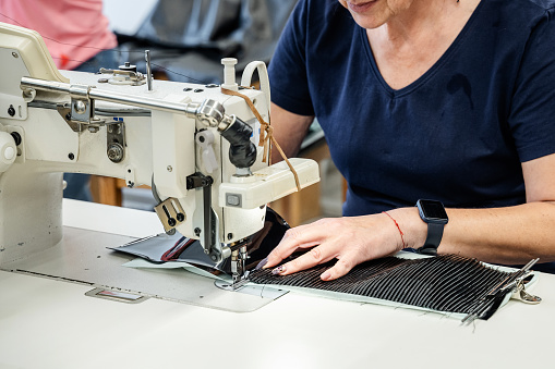 A woman tailor works at a sewing machine sews reuses fabric from old denim clothes. The concept of economical reuse of recyclable things. Homemade needlework hobby. Selective focus