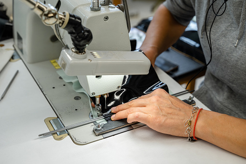 A woman with a beautiful pink manicure sews a homemade protective face mask from fabric. Close-up of a sewing machine and a woman's hands.